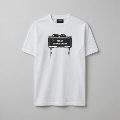 A white short-sleeve crewneck t-shirt with a graphic print of a Claymore Mine that reads 'FRONT TOWARD ENEMY' on the chest, displayed flat against a neutral grey background.