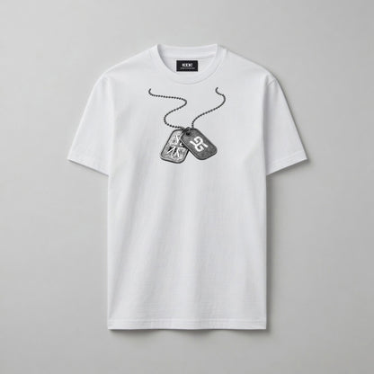 A white short-sleeve crewneck t-shirt featuring a black and grey graphic of military dog tags on a chain across the chest, displayed on a neutral grey background.