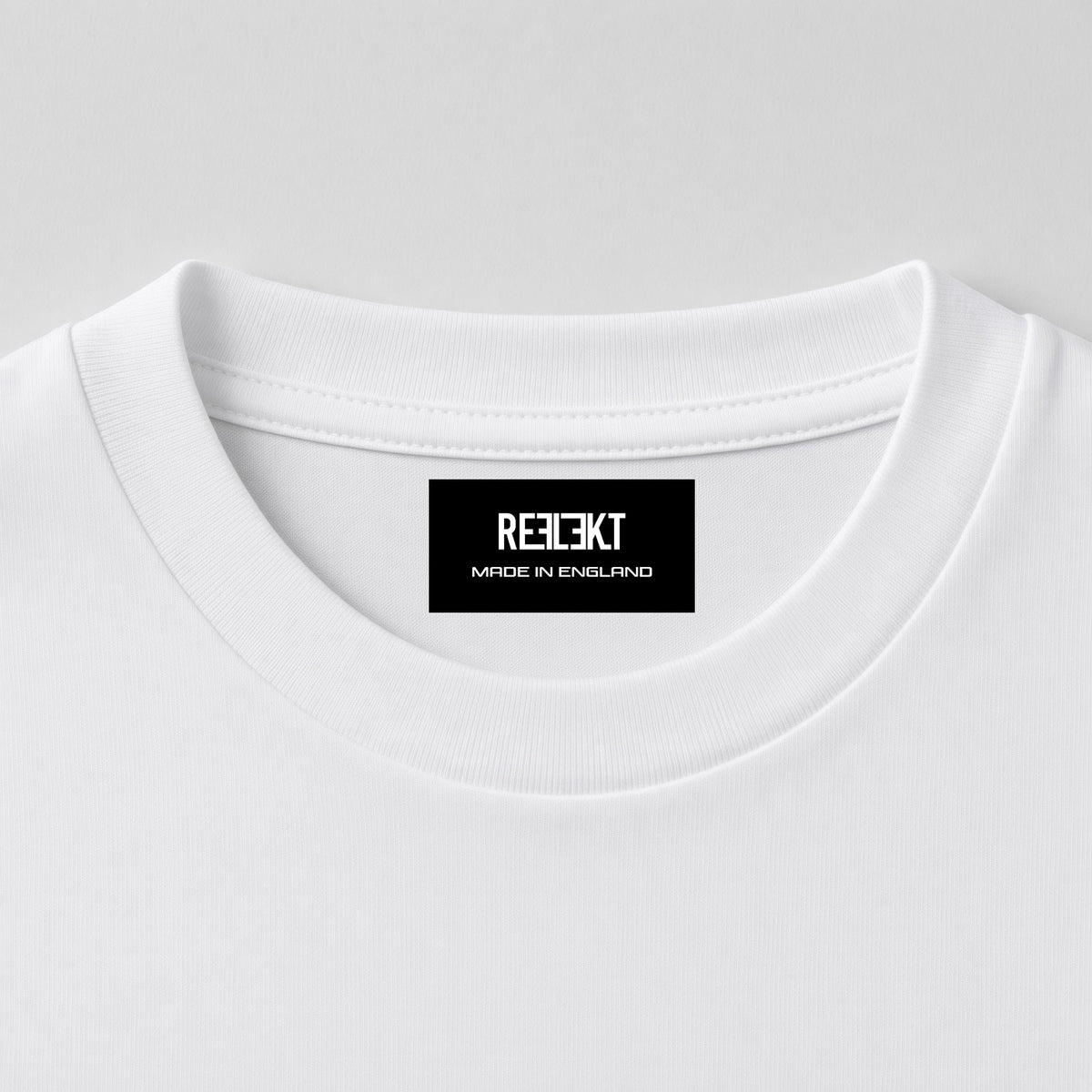Close-up of a white crewneck t-shirt showing the inner neck label with the brand name 'REFLEKT MADE IN ENGLAND' printed in white on a black background.