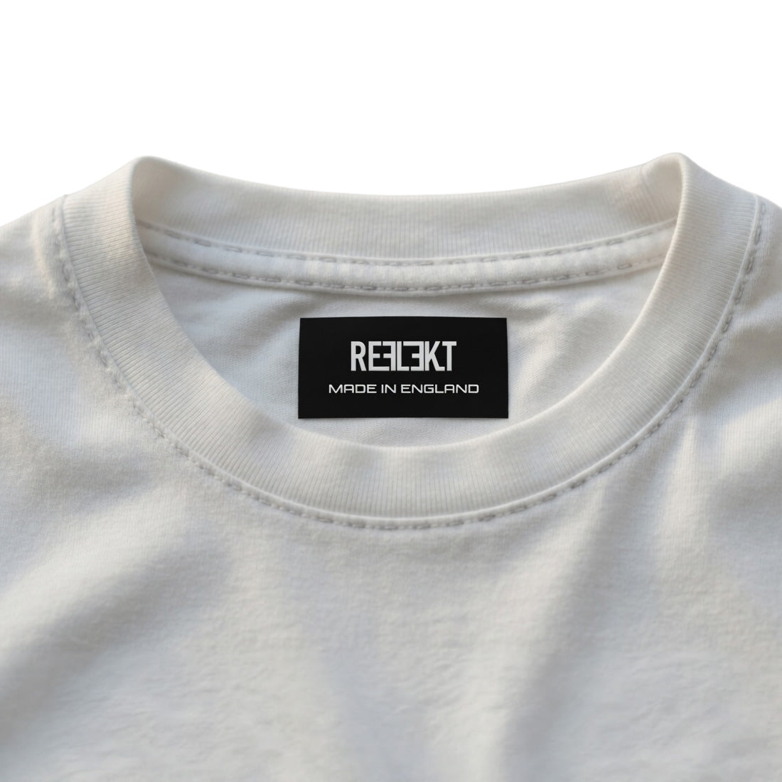 Close-up of a white shirt with a black REFLEKT label on a light gray background